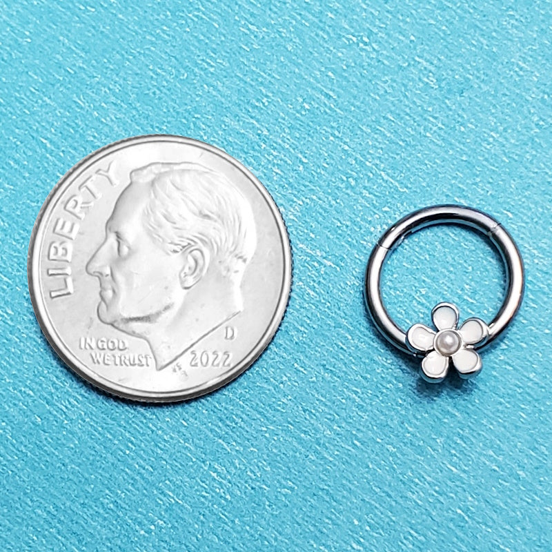 A surgical steel flower septum ring pictured on an aqua background next to a dime for a size comparison.