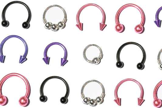 Pink, purple, steel, and black titanium septum rings in rows.