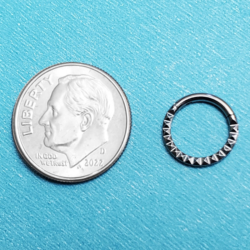 A 16 gauge septum ring pictured on an aqua background next to a dime for a size comparison.