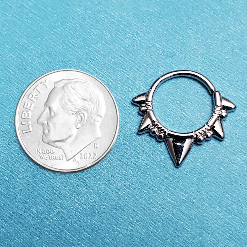 A 16 gauge triangle septum ring pictured on an aqua background next to a dime for a size comparison.