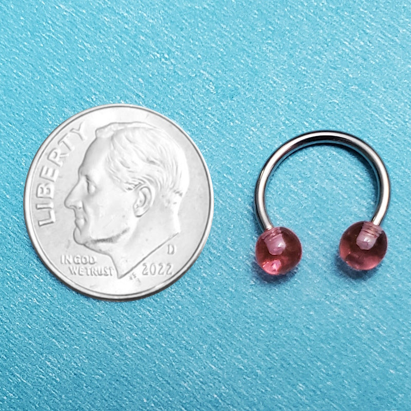 A 16g horseshoe septum ring pictured on an aqua background next to a dime for a size comparison.