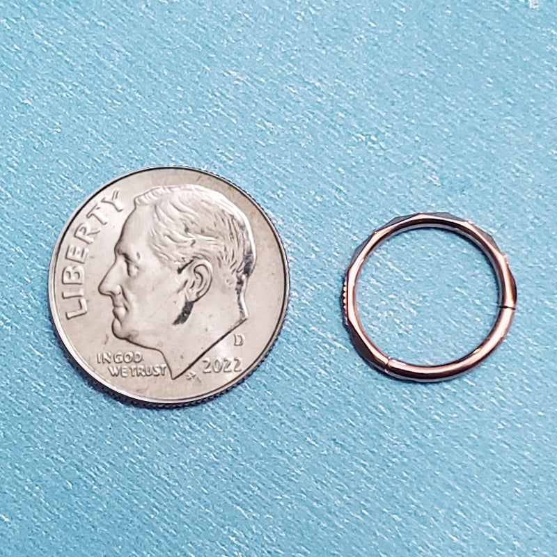 A 16g rose gold septum ring pictured on an aqua background next to a dime for a size comparison.