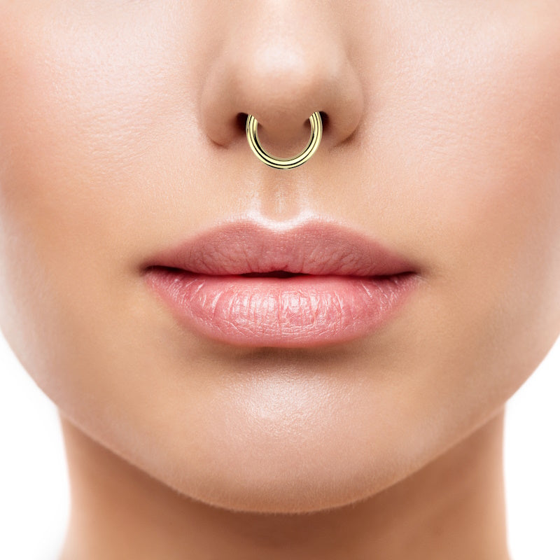 A gold plated 6 gauge segment ring with a hinged segment closure pictured in the septum piercing of a woman.