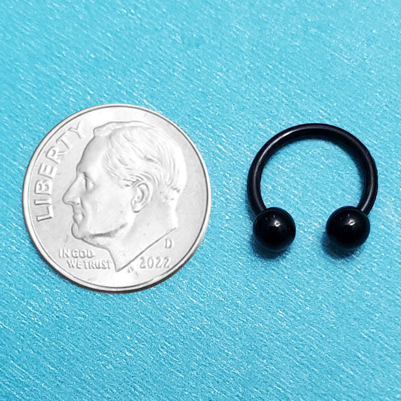 An acrylic black septum ring pictured on an aqua background next to a dime for a size comparison.