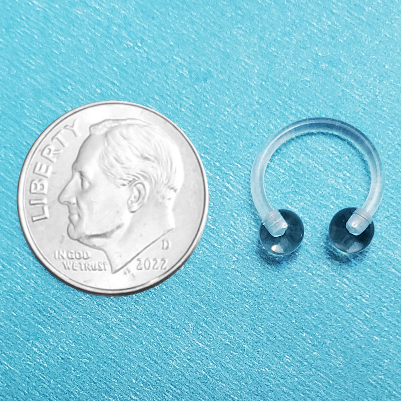 An acrylic clear septum ring pictured on an aqua background next to a dime for a size comparison.