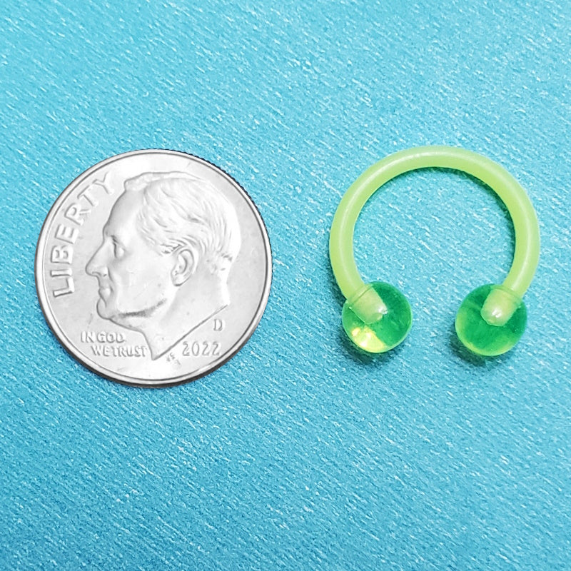 An acrylic green septum ring pictured on an aqua background next to a dime for a size comparison.