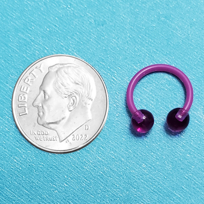 An acrylic purple septum ring pictured on an aqua background next to a dime for a size comparison.