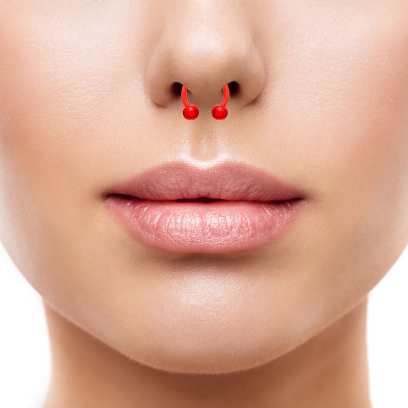 An acrylic red septum ring with a horseshoe shape and a ball on each end pictured in the septum piercing of a woman.