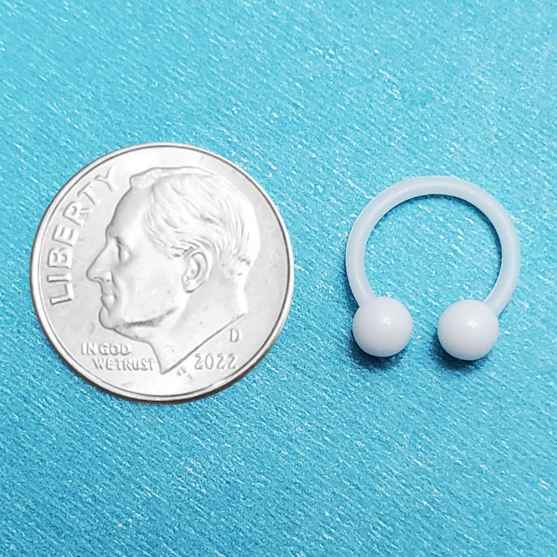 An acrylic white septum ring pictured on an aqua background next to a dime for a size comparison.