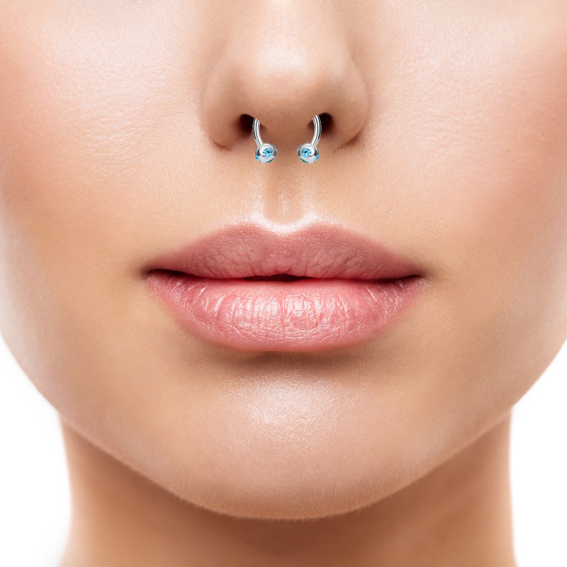 An aqua gem septum ring featuring a horseshoe design with a ball on each end that houses 5 aqua gems pictured in the septum piercing of a woman.