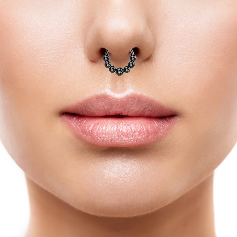 A titanium black bead septum ring with 7 beads around the bottom of the hoop pictured in the septum piercing of a female. 