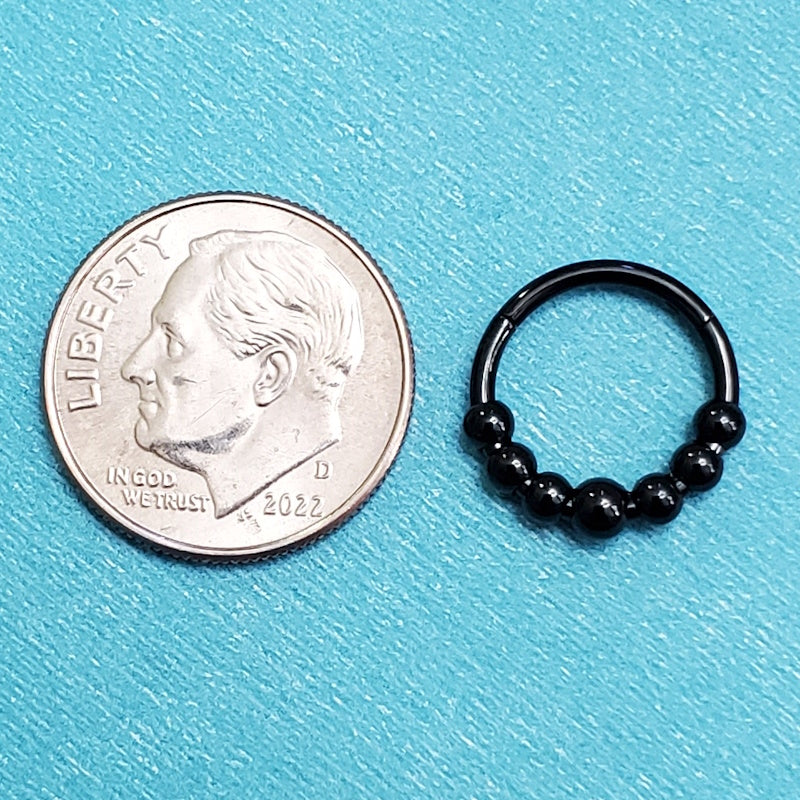 A black bead septum ring pictured on an aqua background next to a dime for a size comparison.