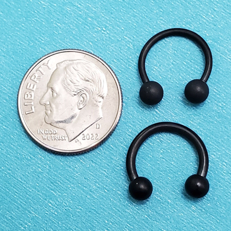 Two sizes of black horseshoe septum rings pictured on an aqua background next to a dime for a size comparison.