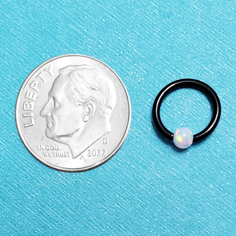 A black opal captive septum ring pictured on an aqua background next to a dime for a size comparison.