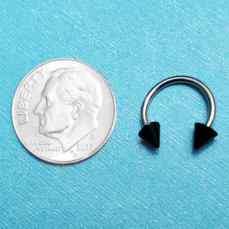 A black spiked horseshoe septum ring pictured on an aqua background next to a dime for a size comparison.