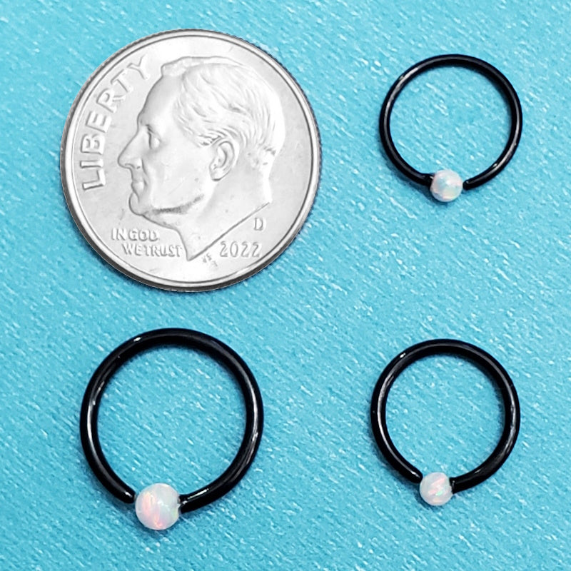 Three sizes of black surgical steel septum rings pictured on an aqua background next to a dime for a size comparison.