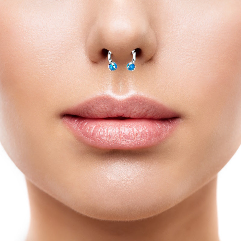 A blue opal septum ring featuring a claw design holding a blue synthetic opal on each end of a horseshoe ring pictured in the septum piercing of a woman.