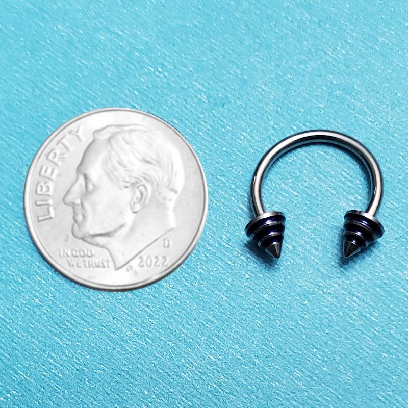 A blue stripe spike septum horseshoe pictured on an aqua background next to a dime for a size comparison.