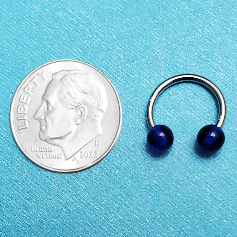 A circular barbell septum piercing ring pictured on an aqua background next to a dime for a size comparison.