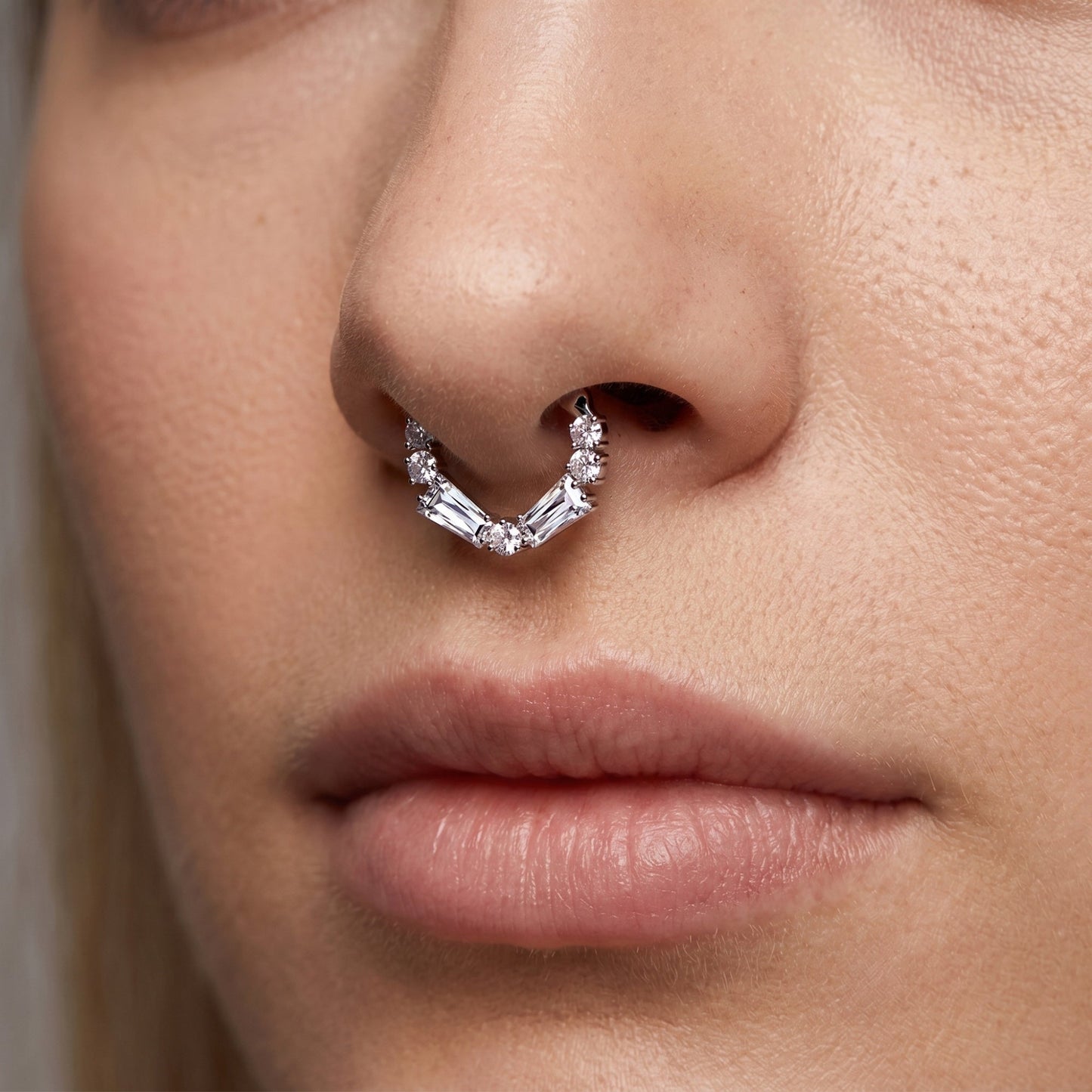 A cubic zirconia septum ring with baguette and round cuts in the septum piercing of a female model.