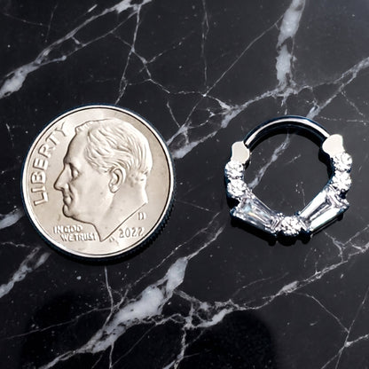 A cubic zirconia septum ring with baguette and round cuts pictured next to a dime for size comparison on a black marble countertop.