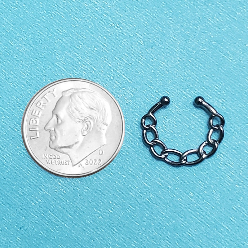 A fake septum nose ring pictured on an aqua background next to a dime for a size comparison.