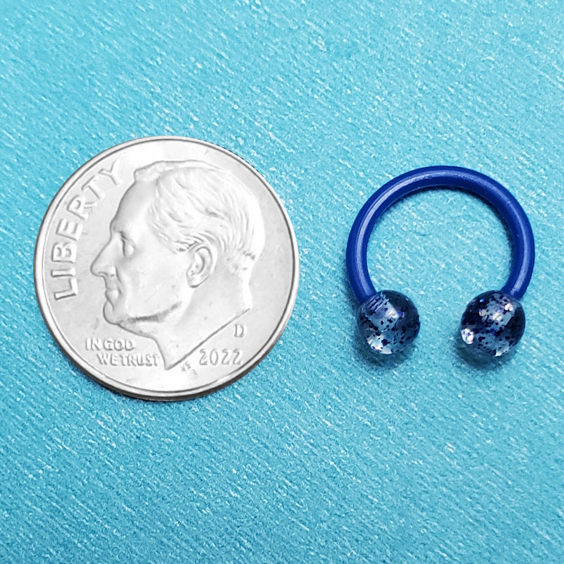 A glitter blue septum ring pictured on an aqua background next to a dime for a size comparison.