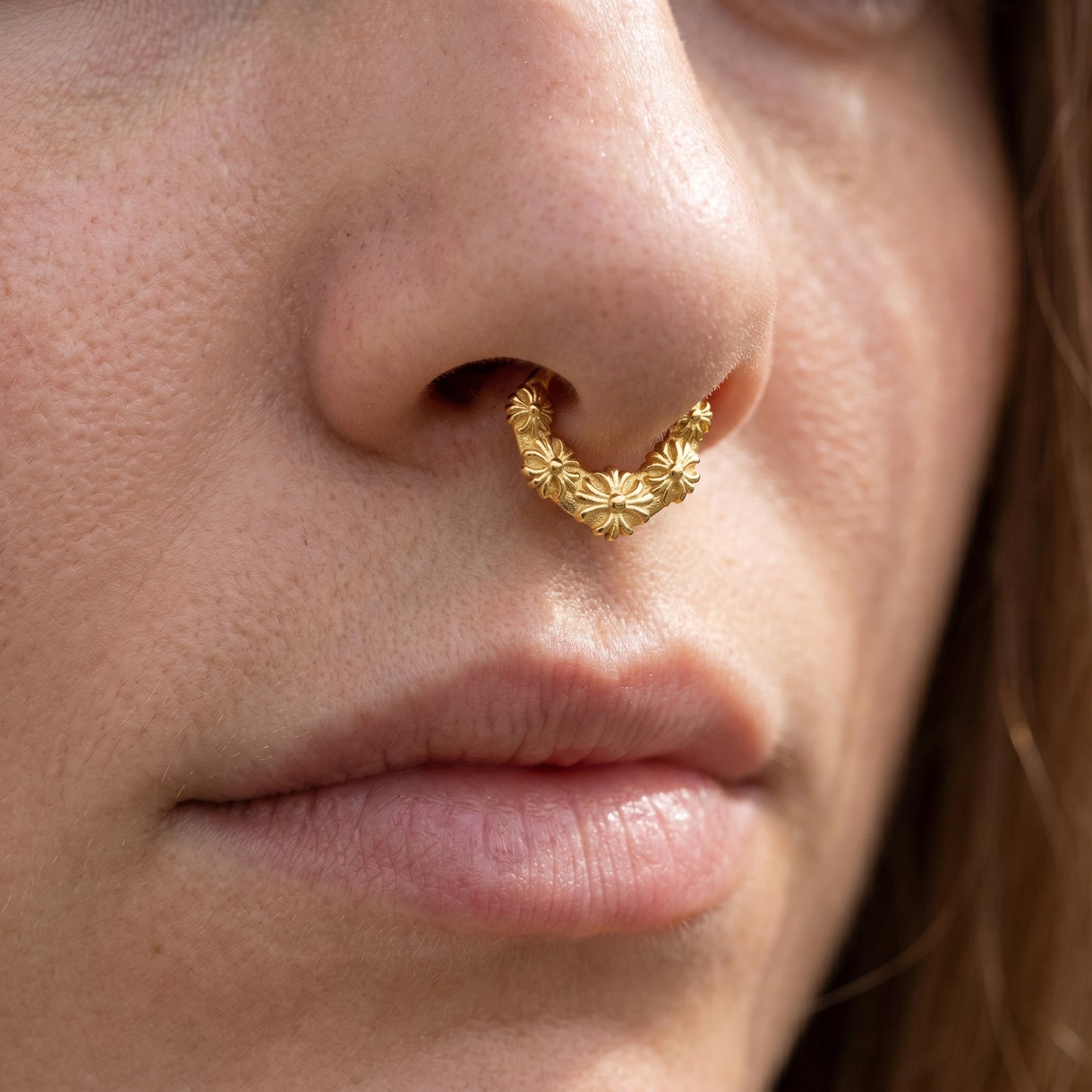 Floral Septum Clicker 16 Gauge Gold Plating Over 316L Surgical Steel pictured in the septum piercing of a female model.