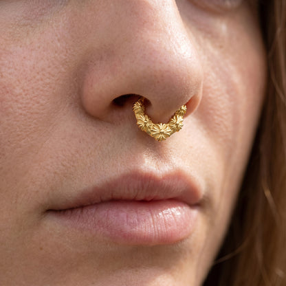 Floral Septum Clicker 16 Gauge Gold Plating Over 316L Surgical Steel pictured in the septum piercing of a female model.