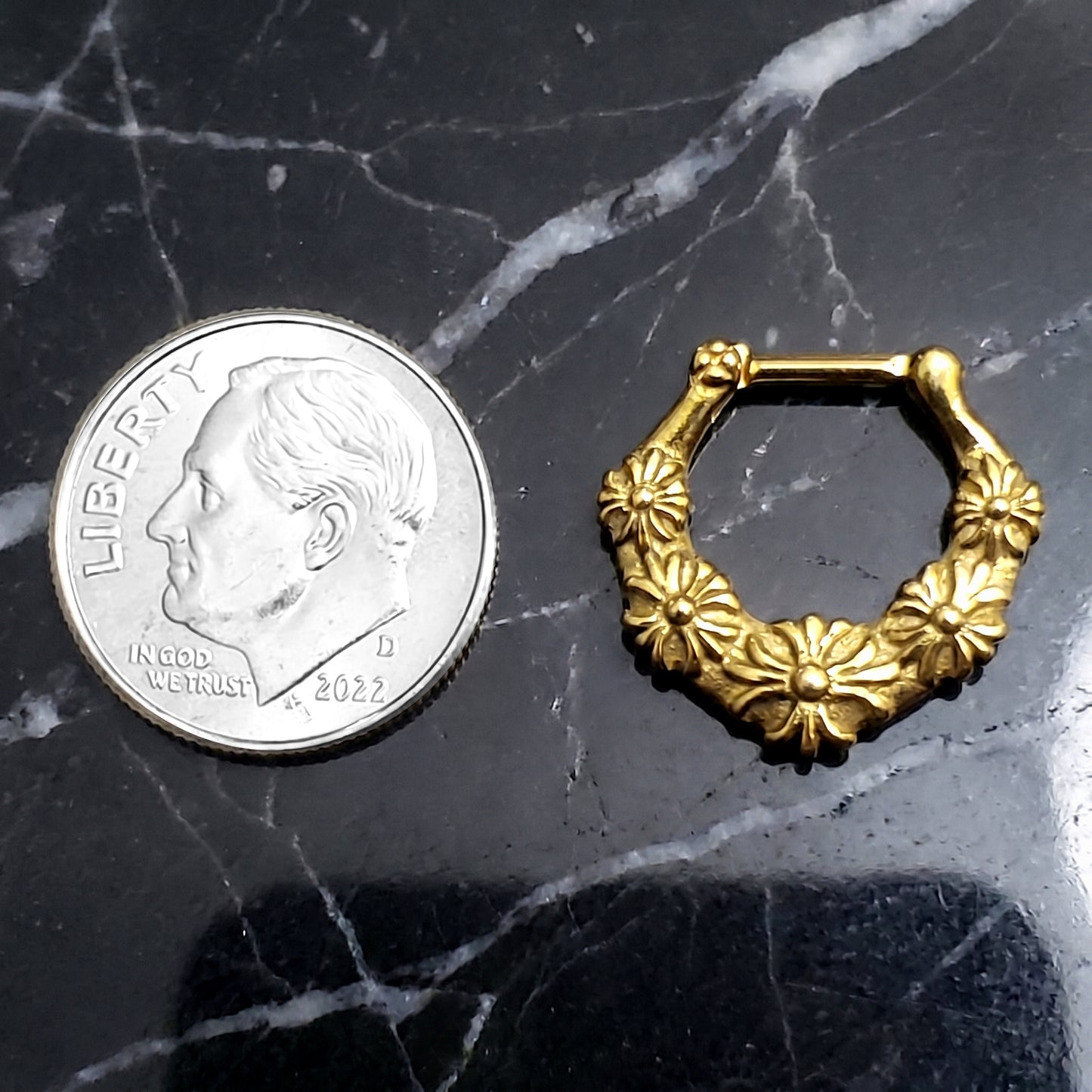 Floral Septum Clicker 16 Gauge Gold Plating Over 316L Surgical Steel pictured on a black marble countertop next to a US dime for size comparison.