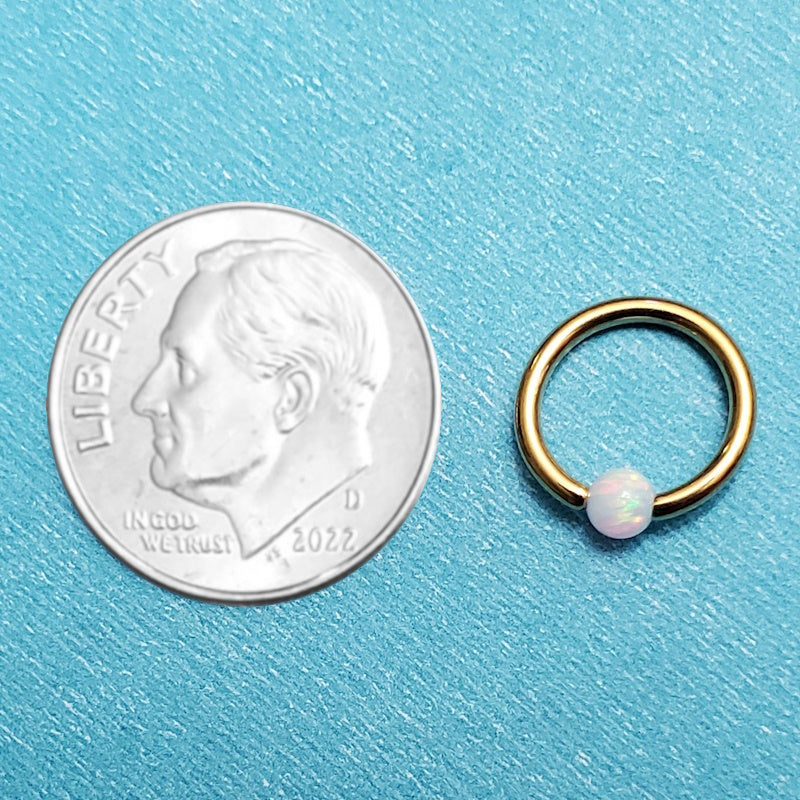 A gold plated opal captive septum ring pictured on an aqua background next to a dime for a size comparison.