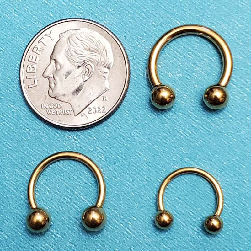 Three sizes of a gold plated septum rings pictured on an aqua background next to a dime for a size comparison.