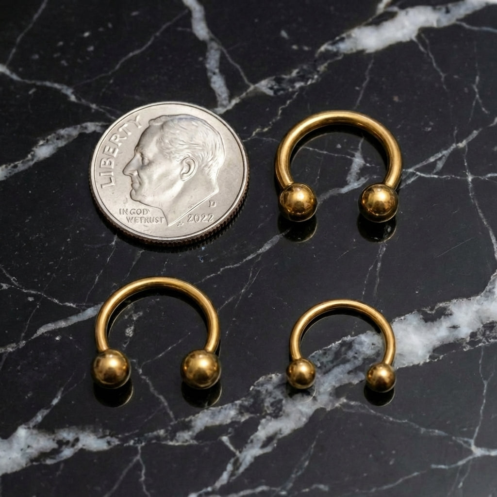 Gold Titanium Septum Ring ASTM F136 Internally Threaded 18G 16G 14G next to a dime for size comparison on a black marble countertop.