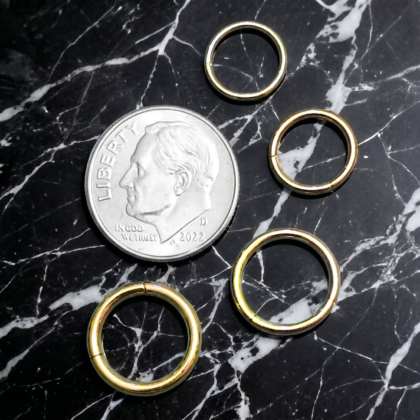 Gold Hinged Segment Septum Hoop ASTM F136 Titanium 20G 18G 16G 14G pictured on a black marble countertop next to a US dime to show size comparison.