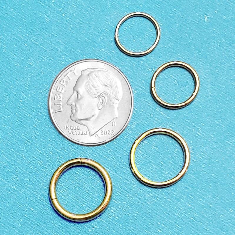 Four sizes of gold titanium septum rings pictured on an aqua background next to a dime for a size comparison.