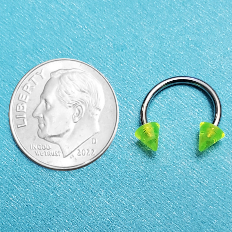 A green spike septum ring pictured on an aqua background next to a dime for a size comparison.