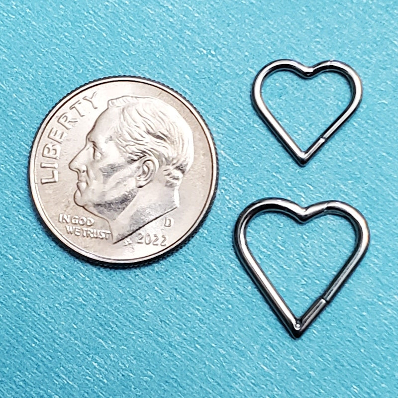 Two sizes of heart shaped septum rings pictured on an aqua background next to a dime for a size comparison.