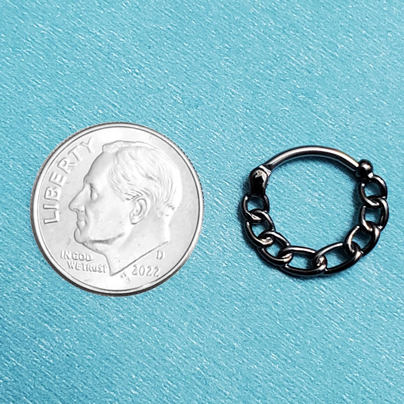 A hematite chain septum ring pictured on an aqua background next to a dime for size comparison.