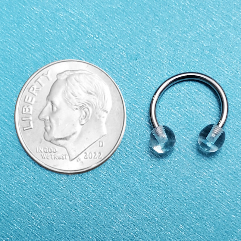 A horseshoe septum nose ring pictured on an aqua background next to a dime for a size comparison.