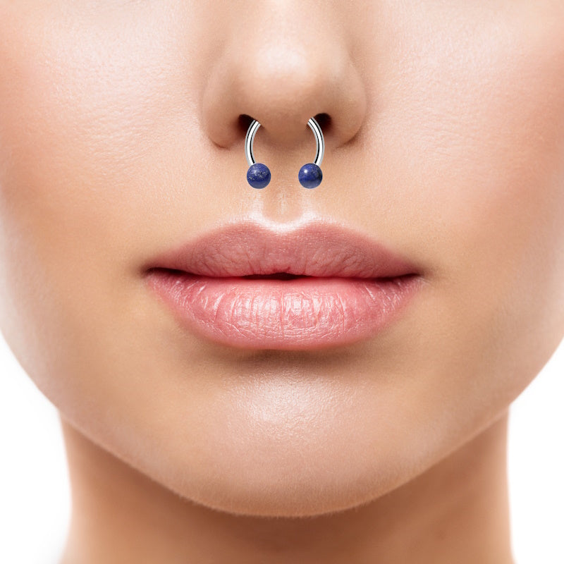 An internally threaded septum ring featuring blue sodalite stones on the end of a horseshoe ring pictured in the septum piercing of a female.