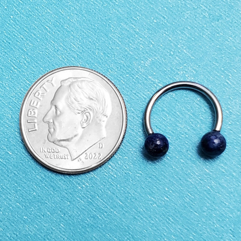 An internally threaded septum ring pictured on an aqua background next to a dime for a size comparison.