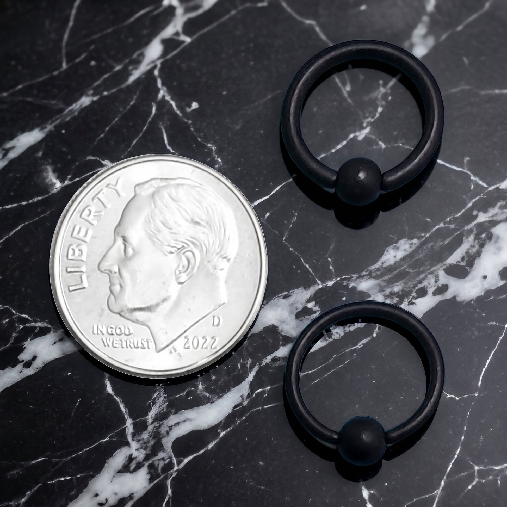 Black Captive Bead Septum Ring 316L Surgical Steel Matte Black 16G 14G pictured next to a US dime for size comparison on a black marble countertop.