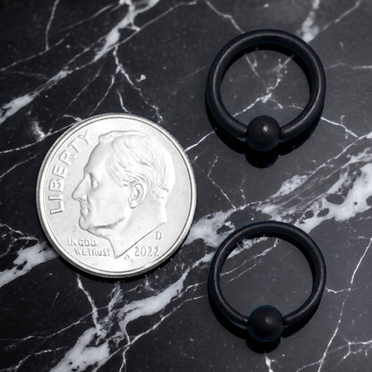 Black Captive Bead Septum Ring 316L Surgical Steel Matte Black 16G 14G pictured next to a US dime for size comparison on a black marble countertop.