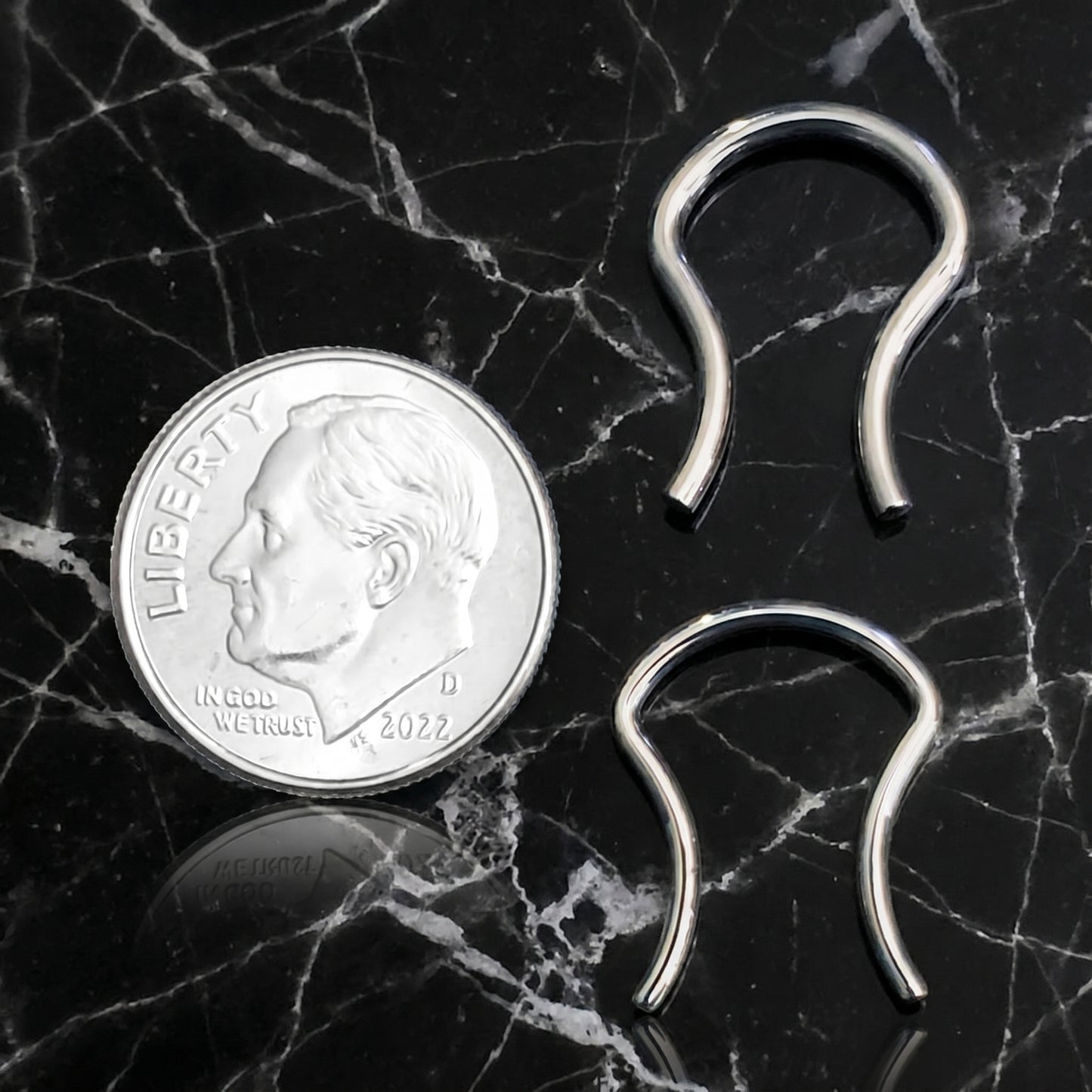 Omega Design Septum Retainer 316L Surgical Steel 16G and 14G pictured next to a US dime for size comparison on a black marble countertop.