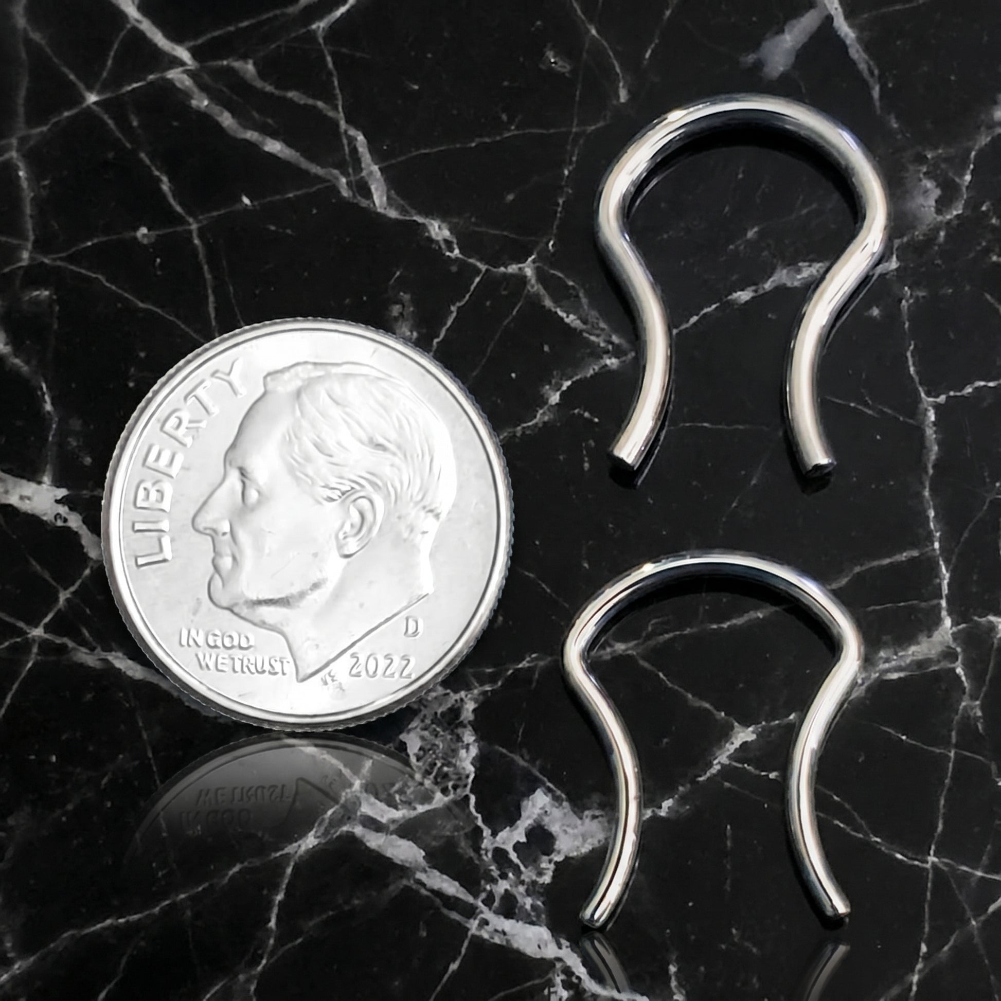 Omega Design Septum Retainer 316L Surgical Steel 16G and 14G pictured next to a US dime for size comparison on a black marble countertop.