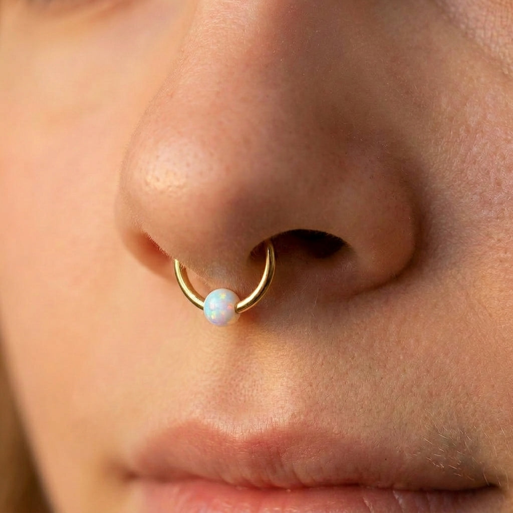 Close-up of a gold septum ring with a central opal on a female model's nose.