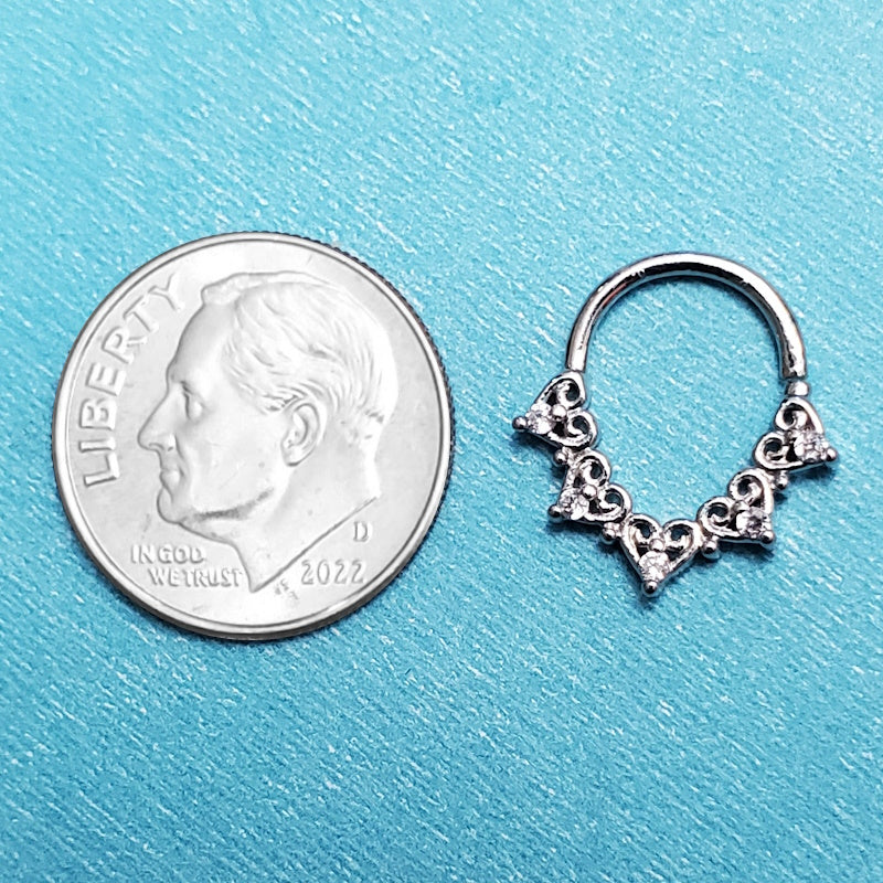 A platinum 18 gauge septum ring pictured on an aqua background next to a dime for a size comparison.