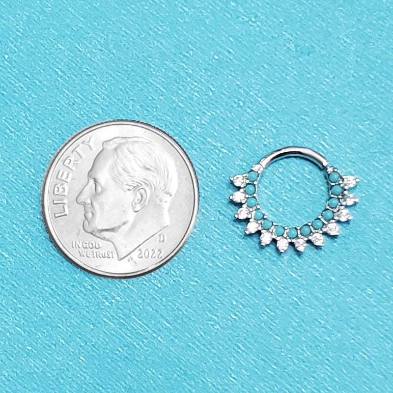 A platinum turquoise septum ring pictured on an aqua background next to a dime for a size comparison.