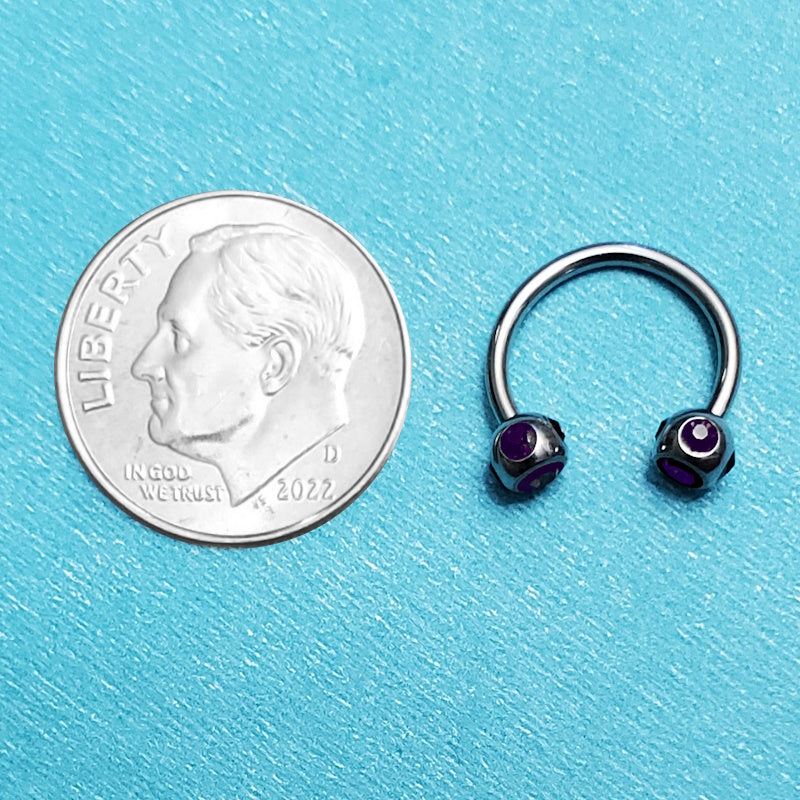 A purple gem septum ring pictured on an aqua background next to a dime for a size comparison.