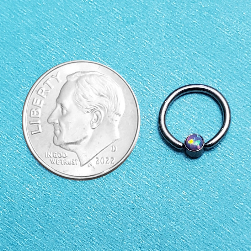 A purple opal septum ring pictured on an aqua background next to a dime for a size comparison.